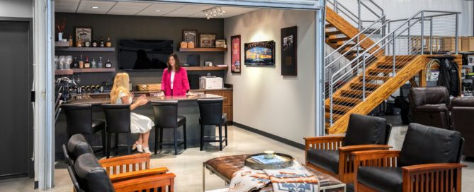 Two women are talking, one is standing and one is sitting at a bar top. They appear to be in a well designed common space.